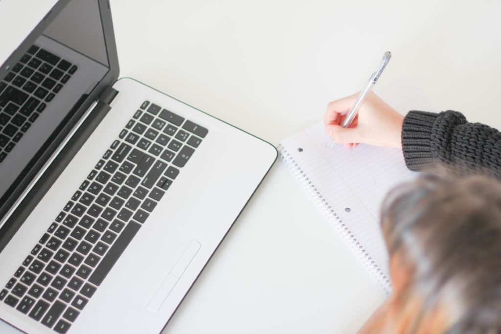 Woman writing in notebook beside laptop